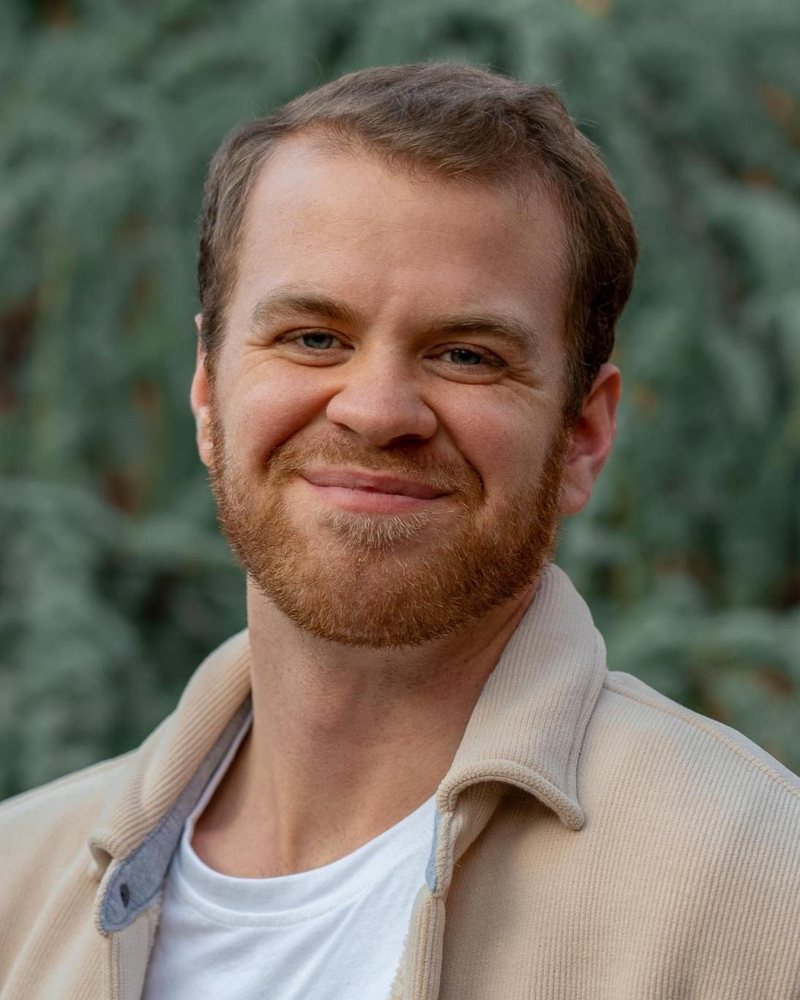 Sam Ahlstrom, smiling, in front of a wall of green leaves
